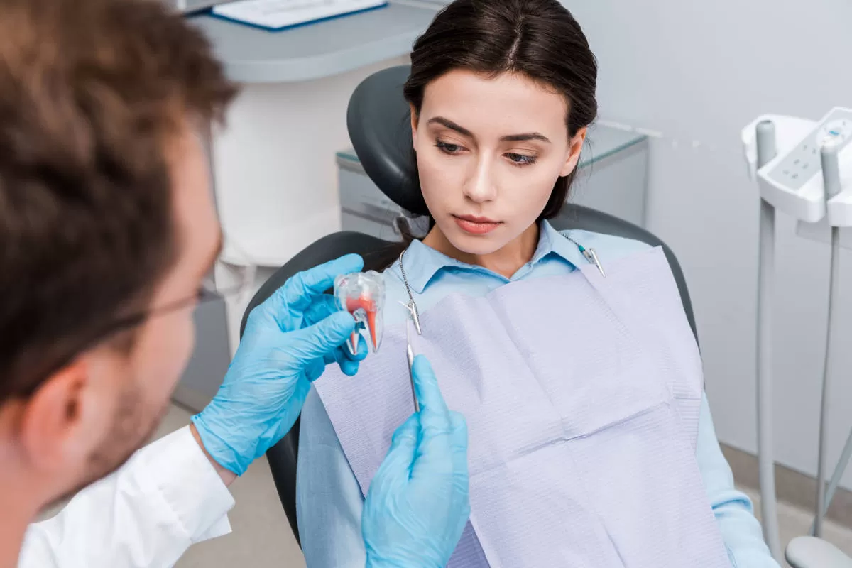 giovane donna dal dentista ascolta spiegazioni del dentista che le mostra il modellino di dente molare