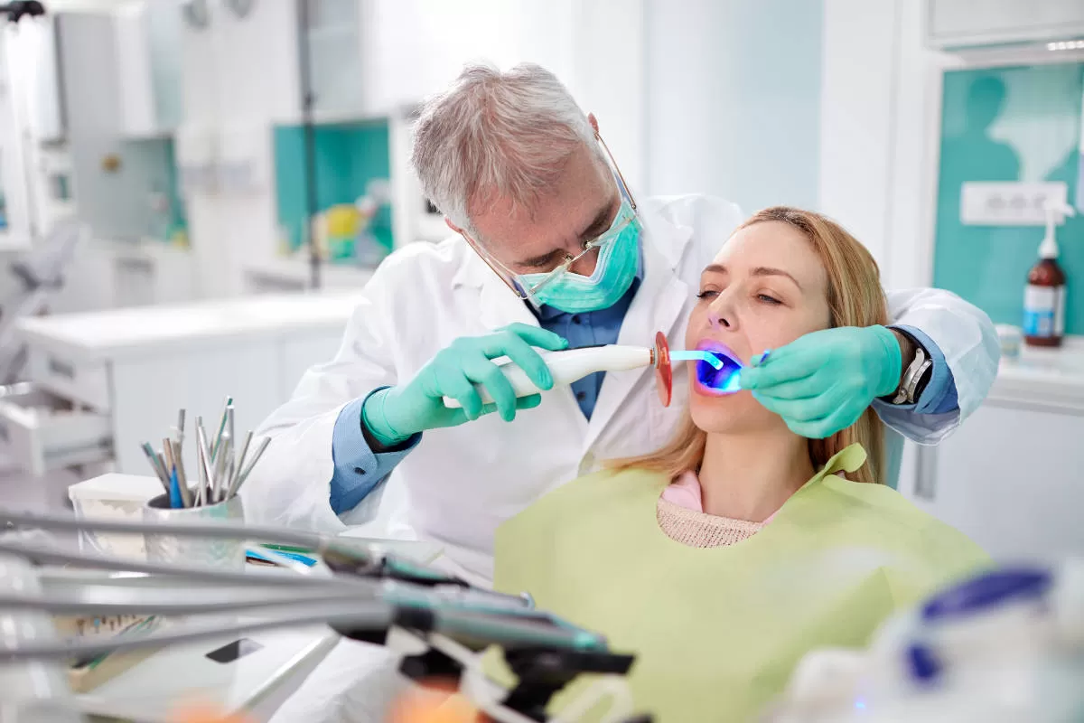 laser dentale dentista con mascherina e guanti di lattice agisce su bocca di paziente seduta in poltrona