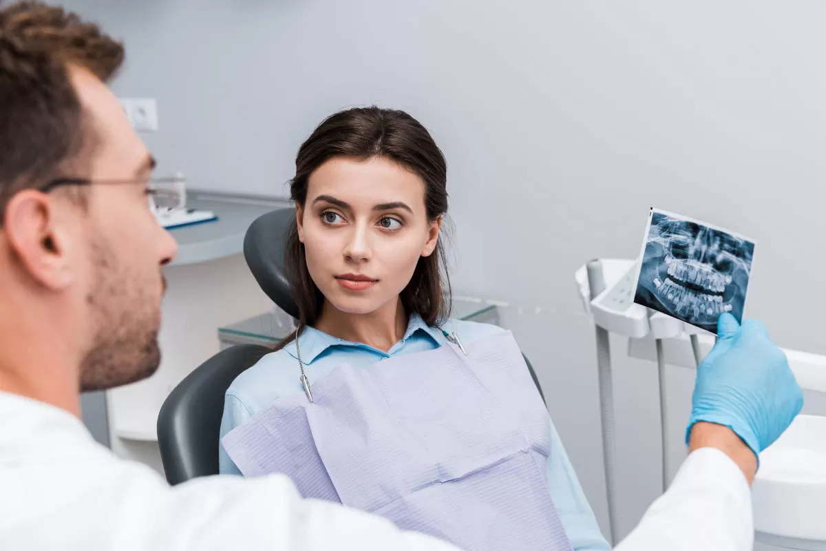 dentista mostra radiografia dentale a giovane donna che ascolta seduta su poltrona del dentista
