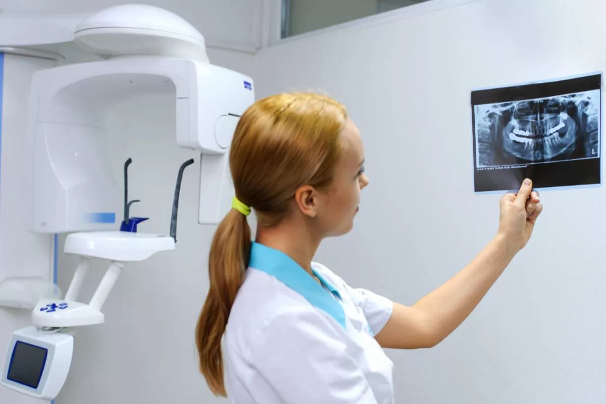 dentista donna con capelli rossi tiene in mano lastra con immagine arcata dentale in uno studio medico