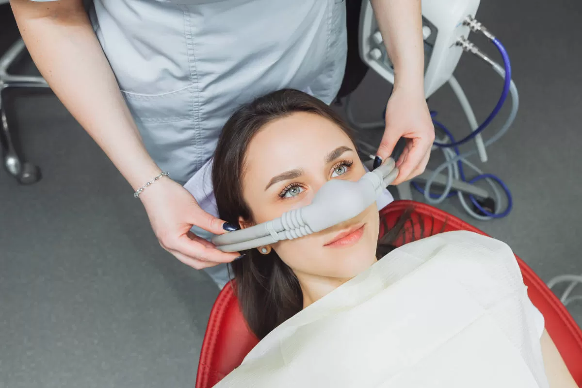 trattamento di sedazione cosciente con strumento su donna giovane con occhi azzurri assistita da personale medico